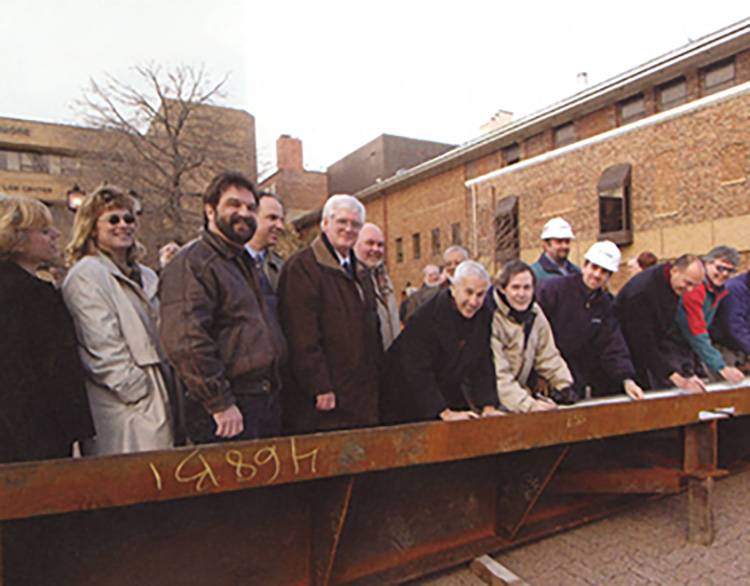 University administration and staff stand around a beam that will be used in the construction of the new Student Center.