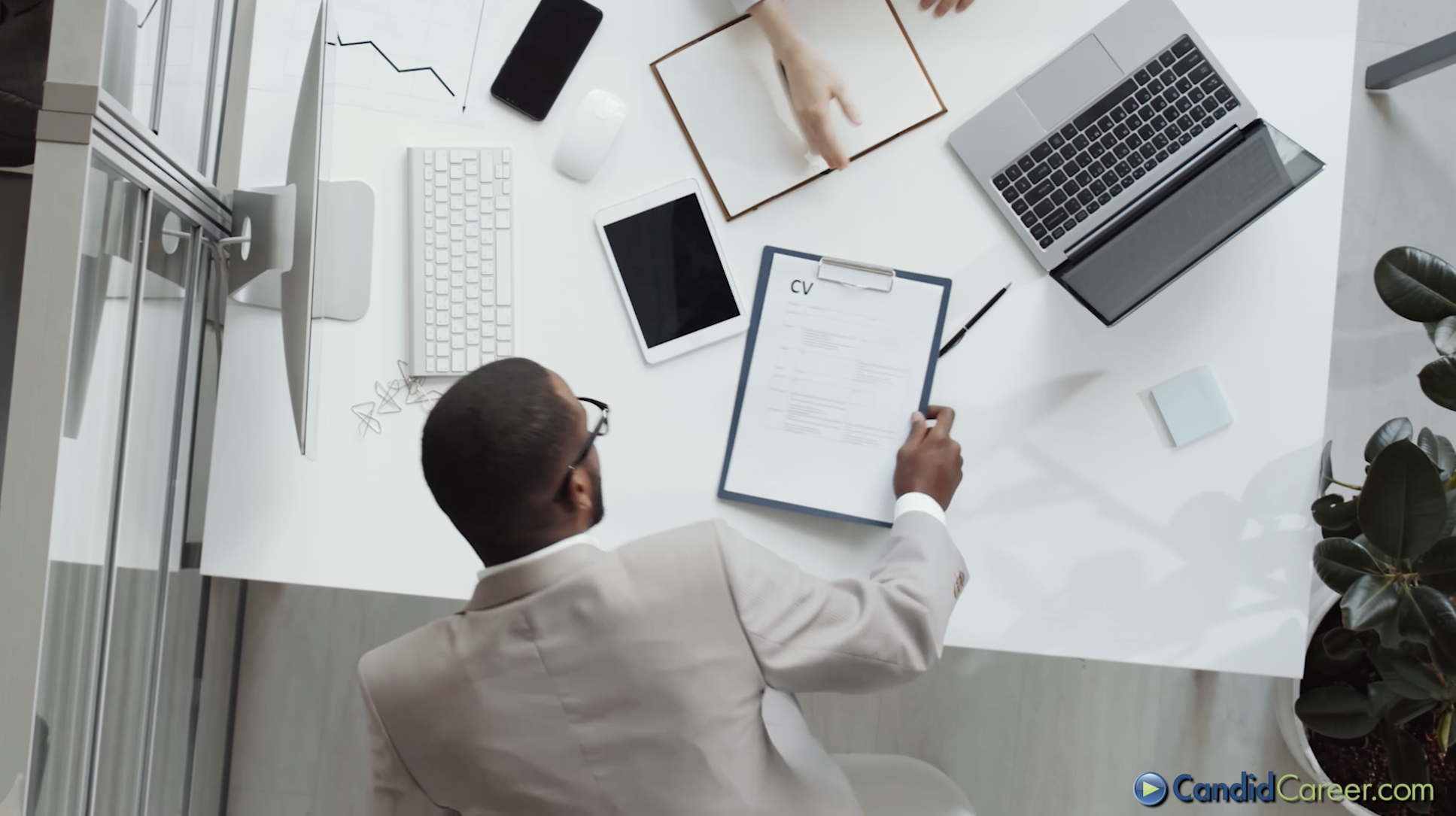 An overhead screenshot of a candidate sitting down at a desk with their CV and a hiring manager.